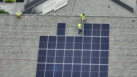 Aerial-shot-of-workers-installing-solar-panels-on-a-shingle-rooftop,-with-arrays-of-panels-already-in-place