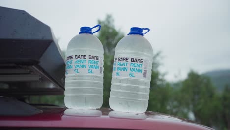 Two-Large-Bottles-of-Water-Placed-on-Top-of-a-Car-in-Sifjord,-Norway---Close-Up