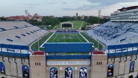 Aufsteigende-Luftaufnahme-Des-Stadions-Der-University-Of-Kansas-Mit-Seinen-Blauen-Sitzen,-Dem-Lebhaften-Spielfeld-Und-Den-Angrenzenden-Campusgebäuden