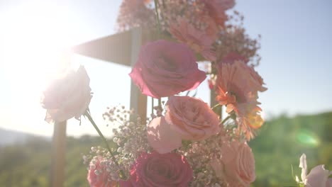 pink-roses-on-golden-wedding-arch,-dolly-shot,-sun-flare-shining,-outdoor-ceremony