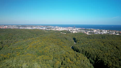 Aerial-backwards-shot-of-dense-forest-with-Gdynia-City-and-Baltic-Sea-in-Background
