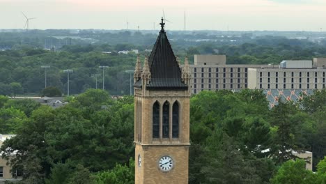 Iconic-Campanile-tower-at-Iowa-State-University,-set-against-lush-greenery,-with-distant-buildings-and-wind-turbines
