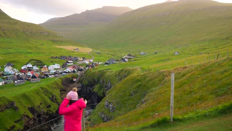 Female-tourist-admiring-Faroese-village-and-nature-on-Atlantic-coast-at-sunset-in-Gjogv,-Faroe-Islands