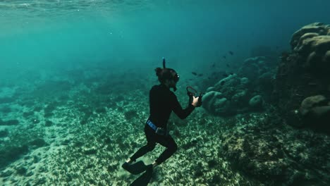 Diver-in-wetsuit-underwater-capturing-media-of-marine-life-and-ascends