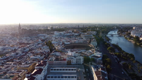 Sunset-aerial-view-of-Plaza-de-Toros,-Guadalquivir-river-and-Seville-Cathedral