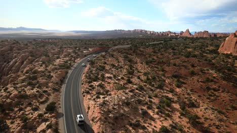 A-panoramic-aerial-view-of-Arches-National-Park,-featuring-a-meandering-road-in-the-center-with-cars-traveling-along-it