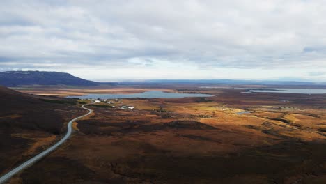 Beautiful-aerial-of-Icelandic-countryside-with-a-lake-in-the-distance-and-a-long-road-running-into-a-small-town