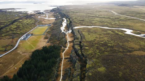 Aerial-of-beautiful-canyon-in-Thingvellir-National-Park-with-distant-waterfall-and-lake-on-a-sunny-day