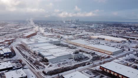 Epic-aerial-winter-shot-of-the-industrial-area-with-steaming-roofs-and-downtown-in-the-background