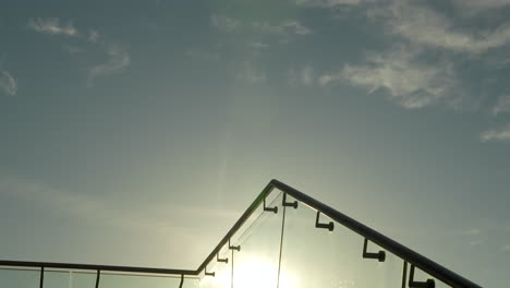 Die-Sonne-Scheint-Durch-Ein-Elegantes-Glasgeländer,-Im-Hintergrund-Die-Silhouette-Von-Masten