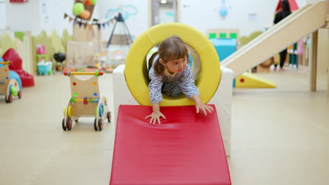 Happy-little-girl-crawls-through-pipe-and-slides-down-at-playroom