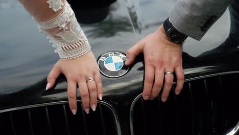 Hands-of-newlyweds-with-wedding-rings-on-hood-of-BMW-car