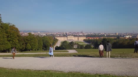 Slow-motion-trucking-shot-of-tourists-at-the-park-of-Schönbrunn-Palace,-observing-the-palace-and-the-cityscape-of-Vienna-on-a-sunny-autumn-morning,-Vienna,-Austria---October-2023