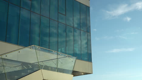 Reflektierende-Gebäudefassade-Unter-Klarem-Himmel-Mit-Modernem-Glasgeländer-Im-Vordergrund