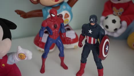 Superhero-figures-amidst-assorted-kids'-toys-on-a-shelf