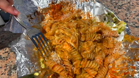 Very-cheesy-pasta-with-green-and-red-pesto,-mixing-pasta-with-a-fork-and-knife,-traditional-Italian-dish,-famous-pasta-in-Puerto-Banus-Marbella,-4K-shot