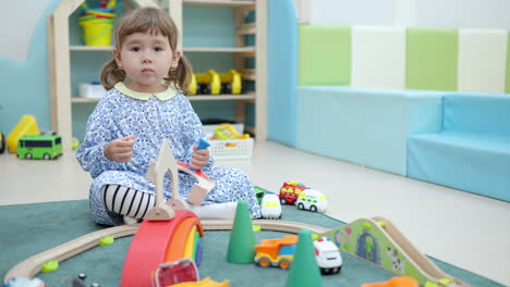 Curious-Little-Girl-with-Pigtails-Playing-with-Toys-and-Looking-Out-What-Other-Kids-Do-on-A-Floor-at-Playroom