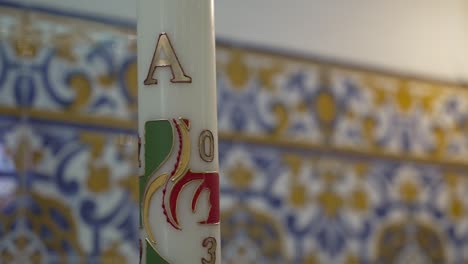 Paschal-candle-in-church-setting,-Decorative-tilework-and-engraved-ceramic-details