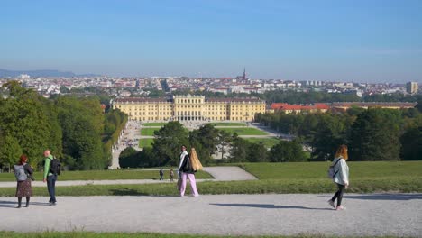 Tourists-walking-at-the-park-of-Schönbrunn-Palace,-observing-the-palace-and-the-cityscape-of-Vienna-on-a-sunny-autumn-morning,-Vienna,-Austria---October-2023