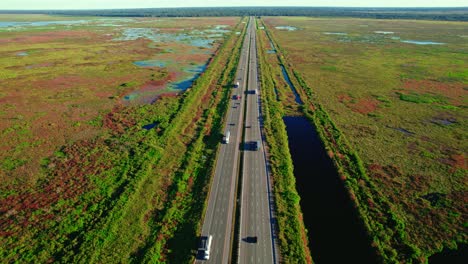 Aerial:-highway-with-adjacent-trucking-rest-stop,-surrounded-by-wetlands