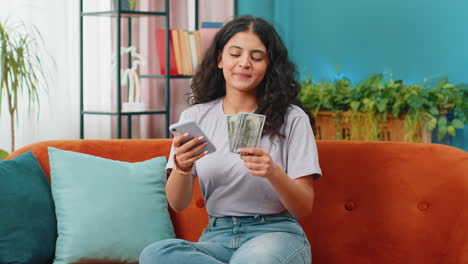 Rich-happy-Indian-woman-counting-money-cash-on-smartphone-calculator-app,-calculate-income-earnings