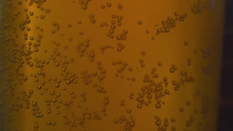 Macro-view-of-bubbles-sticking-to-the-glass-of-a-glass-tumbler,-amber-beer
