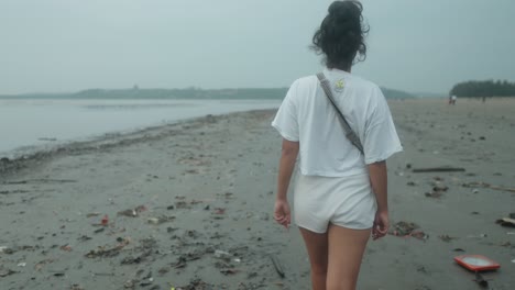 Mujer-Caminando-Sola-En-Una-Playa-Tropical-Con-Basura-Esparcida-En-La-Orilla-Arenosa