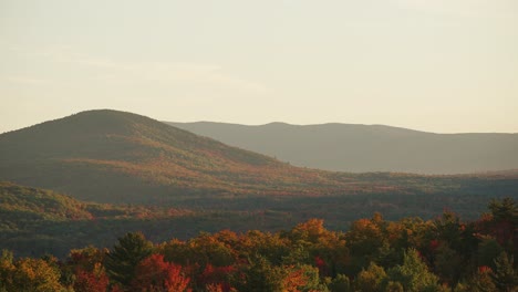 Pan-across-sweeping-view-of-vibrant-red-orange-rolling-hills-during-peak-fall,-White-Mountains-NH