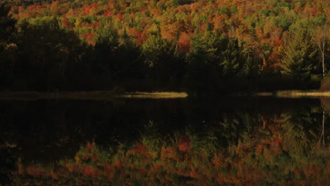 Golden-hour-light-illuminates-sky-and-autumn-foliage-on-mountain-reflection-in-lake