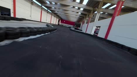 Fpv-racing-drone-flying-over-go-karts-driving-at-high-speed-on-indoor-track-of-kartdrome