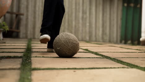 Child-playing-in-a-tiled-yard-with-an-old-football