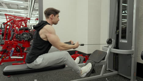 Muscular-Man-Train-Lower-Back-in-Seated-Row-Cable-Machine-in-Modern-Fitness-Center