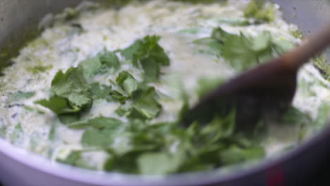 Coriander-being-added-to-a-saucepan-of-coconut-milk