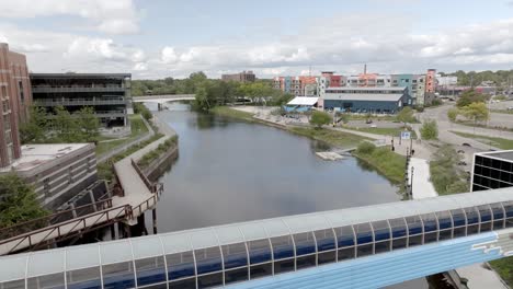 Pedestrian-walkway-over-Grand-River-in-downtown-Lansing,-Michigan-with-drone-video-moving-forward