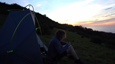 Journaling-man-writing-notebook-in-nature-ocean-campsite-at-sunset