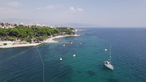 Aerial:-Ovcice-Beach,-Split,-Croatia-with-boats-moored-in-the-clear-blue-sea