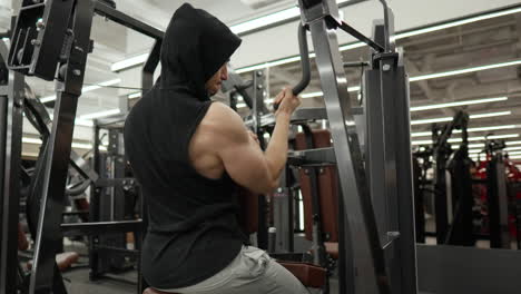 Hombre-Musculoso-Entrenando-Hacia-Atrás-Haciendo-Ejercicio-Con-Una-Mano-En-La-Máquina-En-El-Gimnasio-Moderno