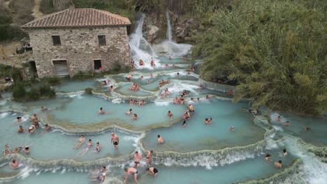 Drone-Flies-Away-from-People-Bathing-in-Saturnia-Thermal-Baths,-Hot-Spring