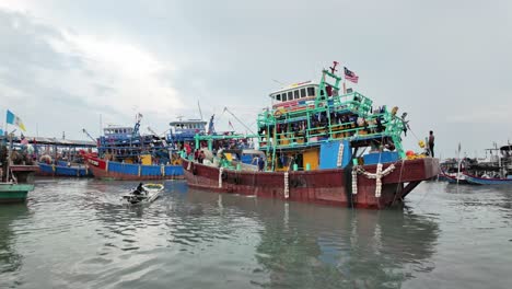 Vibrant-coastal-harbor-with-colorful-fishing-boats,-and-the-Malaysian-flag-indicating-location-against-an-overcast-sky