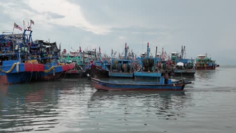Vibrant-coastal-harbor-with-colorful-fishing-boats,-and-the-Malaysian-flag-indicating-location-against-an-overcast-sky