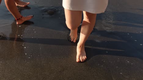 Female-feet-walk-of-black-sand-beach,-engulfed-by-small-white-waves