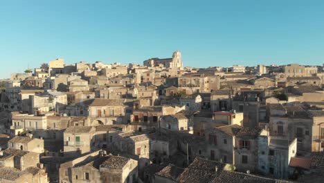 Flying-low-over-barogue-city-Modica-during-sunrise-and-blue-sky,-aerial