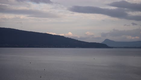 Lake-Annecy-on-overcast-day-in-the-French-Alps-with-far-mountains,-Pan-right-shot