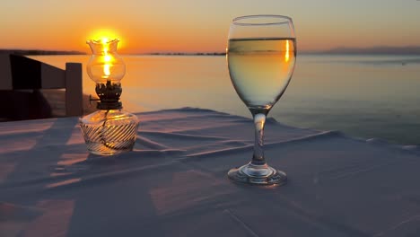 Vintage-table-oil-lamp-and-glass-of-wine-against-sunset-backdrop