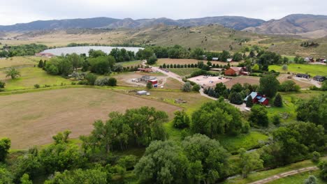 Atemberaubendes-Drohnenvideo,-Das-Die-Atemberaubende-Landschaft-Colorados-Zusammen-Mit-Einem-See-Und-Einem-Ackerland-Mit-Bezaubernden-Hütten-Und-Majestätischen-Bergen-Zeigt
