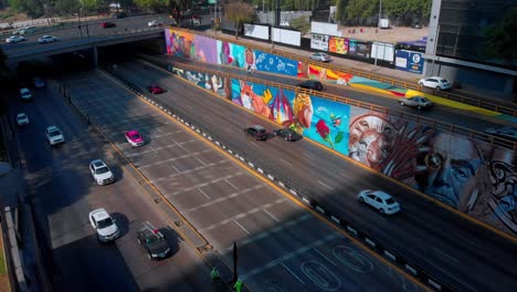 Drone-ascending-Mexico-city-highway-street-art-murals-colorful-painting-shadow-and-daylight-cars-speed-intersection
