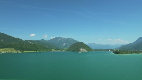 Eine-Filmische-Drohne-Fliegt-über-Dem-Wasser-Und-Offenbart-österreichische-Pracht:-Den-Ruhigen-Wolfgangsee,-Umrahmt-Von-Fernen-Majestätischen-Bergen,-übersät-Mit-Schilfbedeckten-Inseln