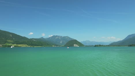 Cinematic-drone-gracefully-glides-low,-revealing-Austrian-splendor:-the-tranquil-Wolfgangsee-lake-framed-by-distant-majestic-mountains,-dotted-with-reed-covered-islands
