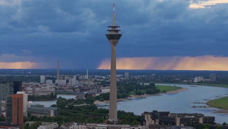 Rhine-tower-Dusseldorf-with-storm-clouds-on-horizon,-telephoto-drone-shot