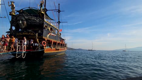 Llegada-Aventurera:-Viajeros-Emocionados-Desembarcando-De-Un-Barco-Pirata-En-El-Muelle-De-Saranda,-Abrazando-La-Belleza-Costera-Junto-Al-Mar